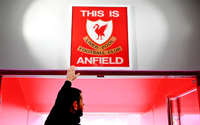 Hand touching "This is Anfield" sign at Liverpool FC's Anfield Stadium.