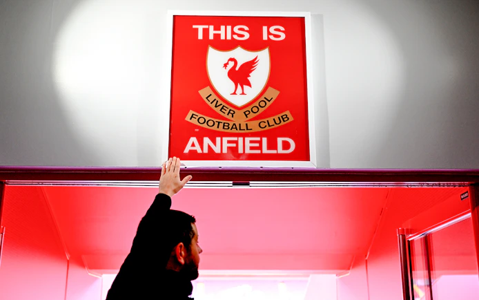 Hand touching "This is Anfield" sign at Liverpool FC's Anfield Stadium.