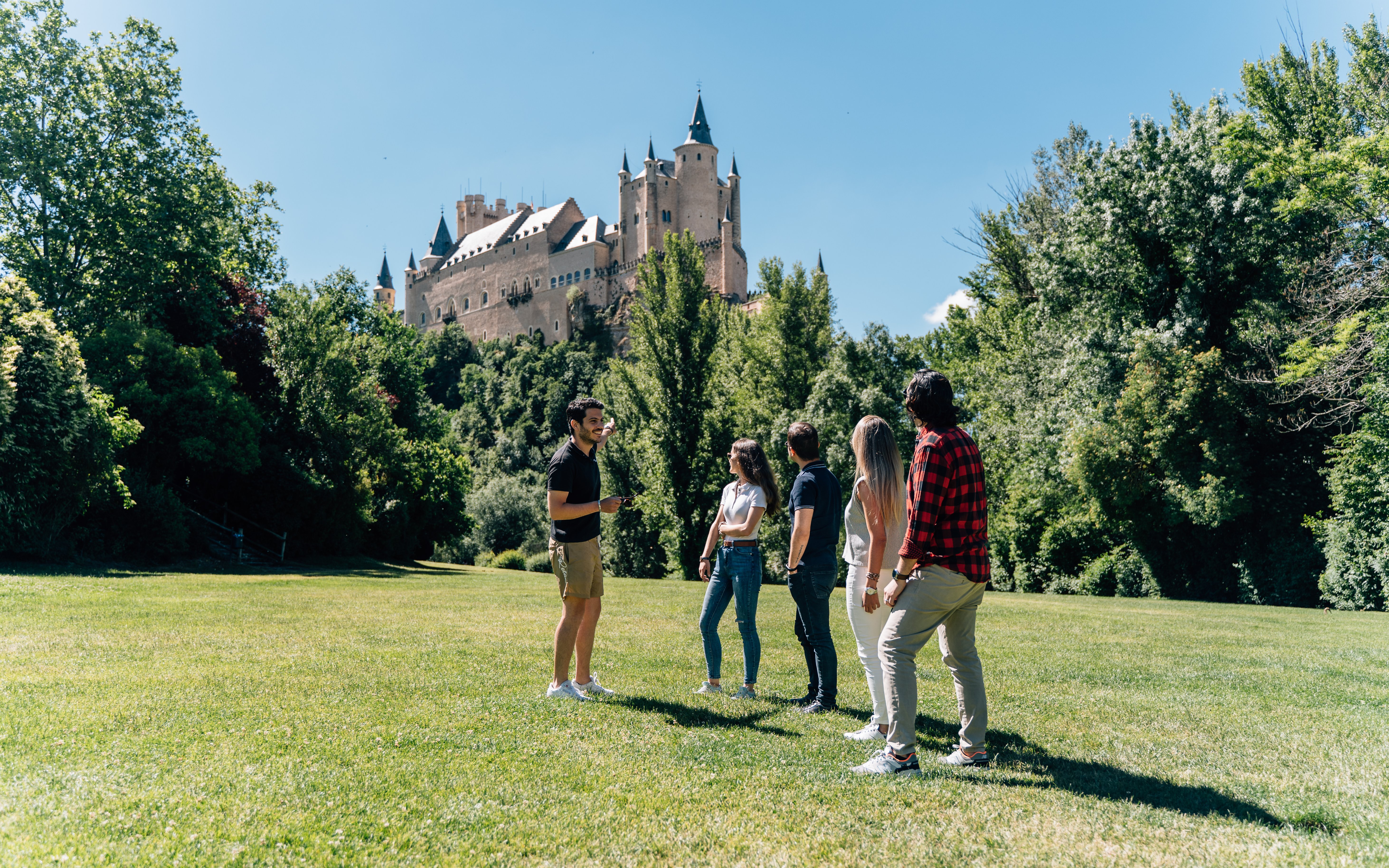 Guided tour group viewing the Alcázar of Segovia in a lush green setting.