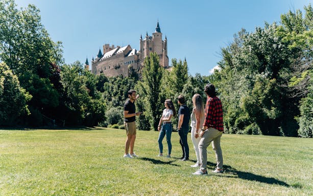 Guided tour group viewing the Alcázar of Segovia in a lush green setting.
