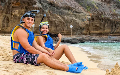 Guests in snorkeling gear sitting on Hanauma Bay beach, ready for snorkeling tour.