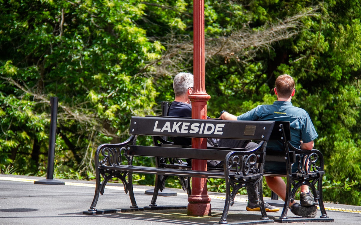 Two people sitting on a bench at Lakeside station platform during Puffing Billy tour.