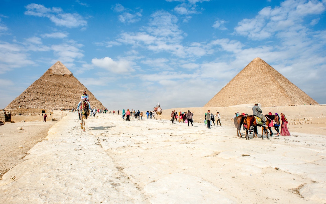 Tourists and camels at the Giza Complex with pyramids in the background.