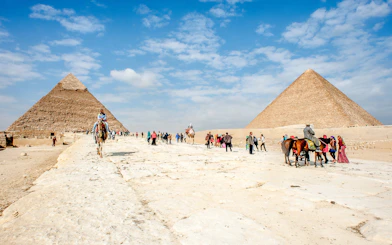 Tourists and camels at the Giza Complex with pyramids in the background.