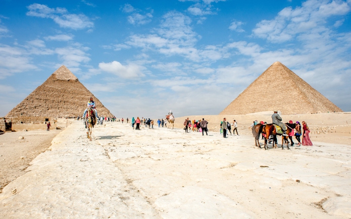 Tourists and camels at the Giza Complex with pyramids in the background.