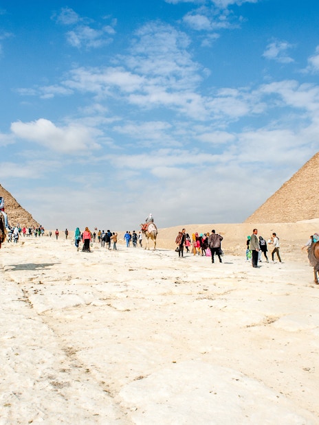 Tourists and camels at the Giza Complex with pyramids in the background.