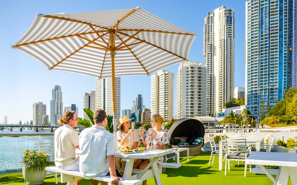 Four guests dining under an umbrella on a top deck with Surfers Paradise skyline in the background.