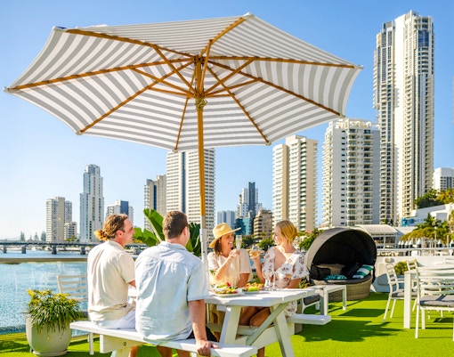 Four guests dining under an umbrella on a top deck with Surfers Paradise skyline in the background.