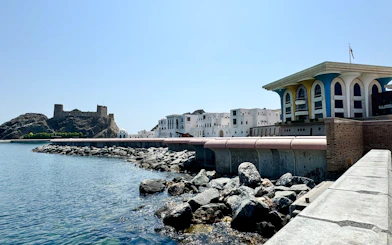 Coastal view of Al Alam Palace and rocky shoreline in Old Muscat, Oman.