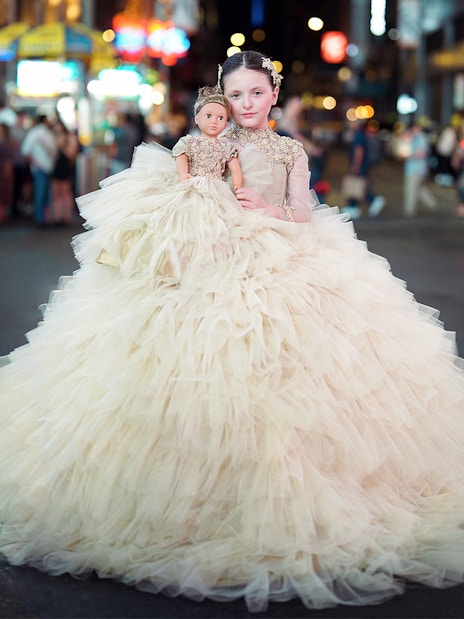 Girl in a formal dress holding a matching doll on a city street at night.