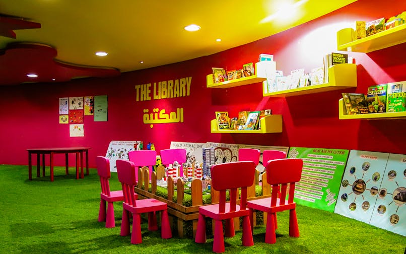 Children's reading area in a colorful library with books on shelves and small chairs around a table.