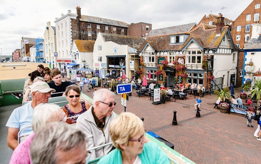 Open-top bus tour in Bournemouth passing through a lively street with cafes and historic buildings.