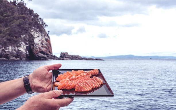 Plate of fresh salmon sashimi held by the ocean in Tasmania.