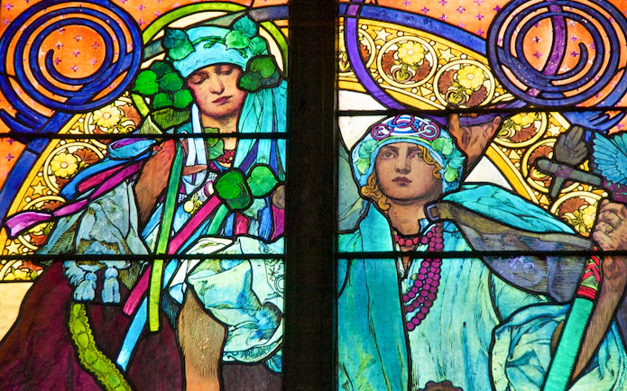 Stained glass window detail at Prague Castle, featuring vibrant figures and intricate patterns.
