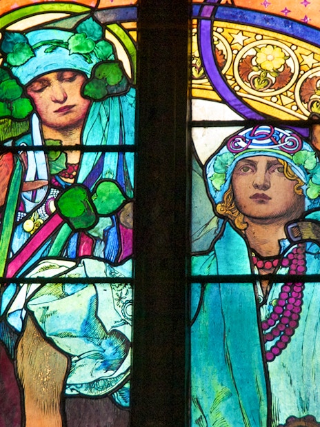 Stained glass window detail at Prague Castle, featuring vibrant figures and intricate patterns.