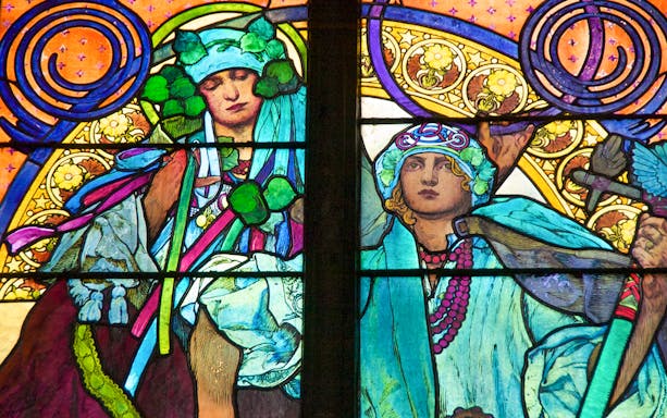 Stained glass window detail at Prague Castle, featuring vibrant figures and intricate patterns.