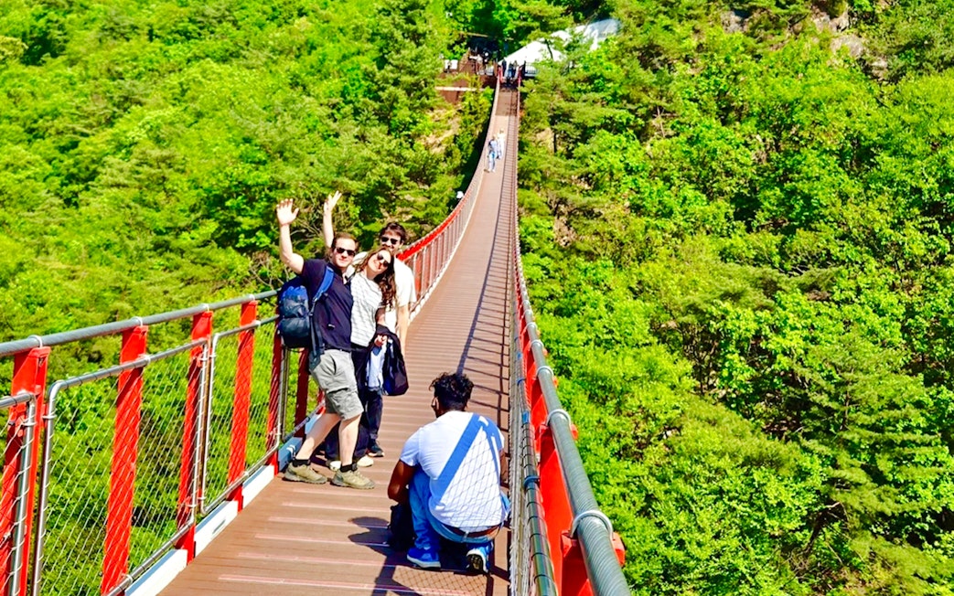 Tourists on a red suspension bridge enjoying mountain views during a DMZ tour from Seoul.