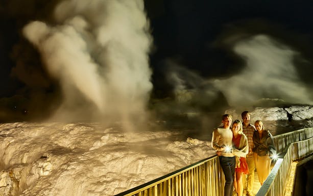 Visitors on a night tour of Te Puia Geysers, New Zealand, with steam rising in the background.