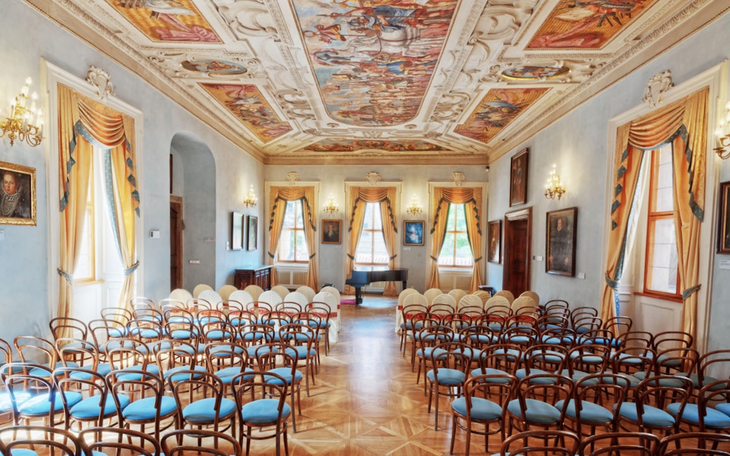 Lobkowicz Palace Museum hall with ornate ceiling and empty chairs in Prague.