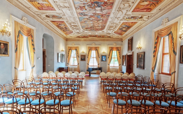 Lobkowicz Palace Museum hall with ornate ceiling and empty chairs in Prague.