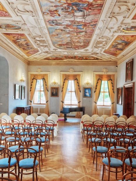 Lobkowicz Palace Museum hall with ornate ceiling and empty chairs in Prague.