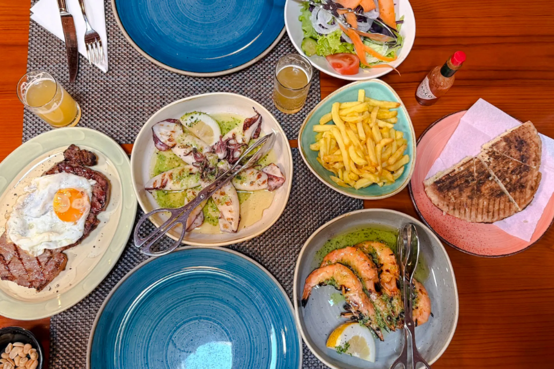 Traditional Madeira cuisine with grilled seafood, steak, fries, salad, and bread on a dining table.
