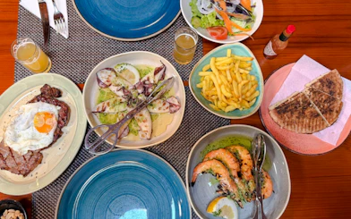 Traditional Madeira cuisine with grilled seafood, steak, fries, salad, and bread on a dining table.