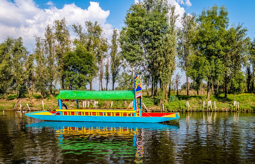Trajinera boat with colorful decorations on Xochimilco canal, Mexico City, featuring lively group celebration.