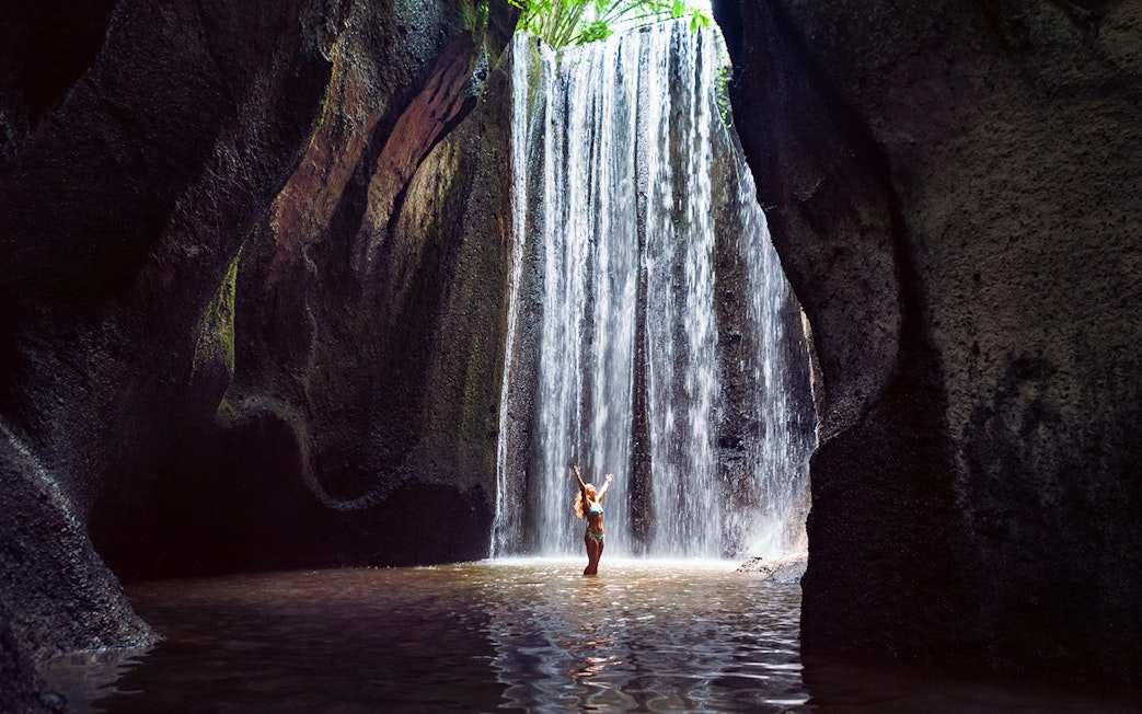 Waterfall in Bali with person standing beneath, part of Mount Batur Jeep Tour.