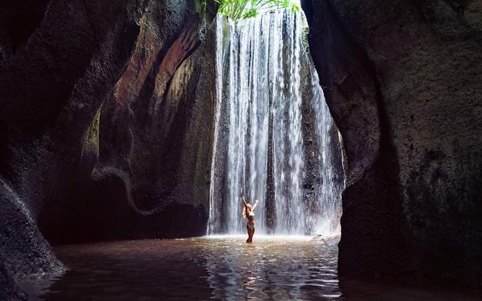 Waterfall in Bali with person standing beneath, part of Mount Batur Jeep Tour.