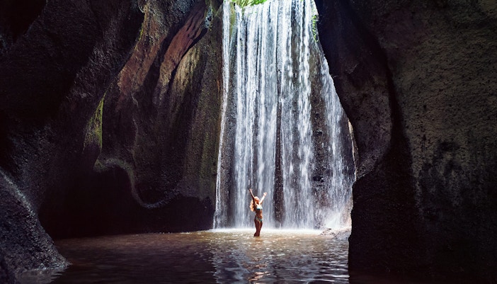 Waterfall in Bali with person standing beneath, part of Mount Batur Jeep Tour.