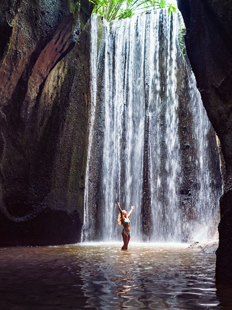 Waterfall in Bali with person standing beneath, part of Mount Batur Jeep Tour.