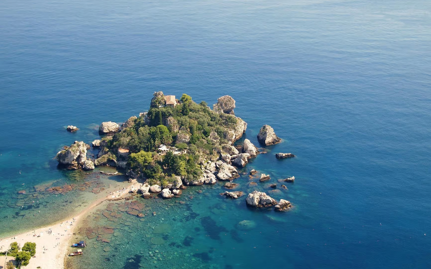 Aerial view of Isola Bella Island surrounded by clear blue sea, featuring rocky coastline and lush greenery.