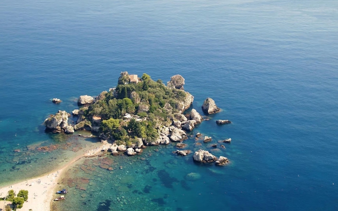 Aerial view of Isola Bella Island surrounded by clear blue sea, featuring rocky coastline and lush greenery.