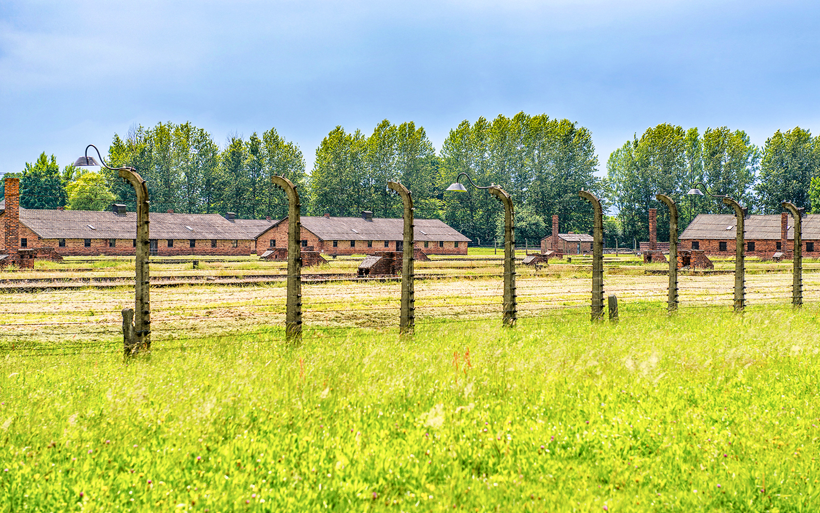 Auschwitz-Birkenau barracks and barbed wire fence under a blue sky, part of Krakow tour.