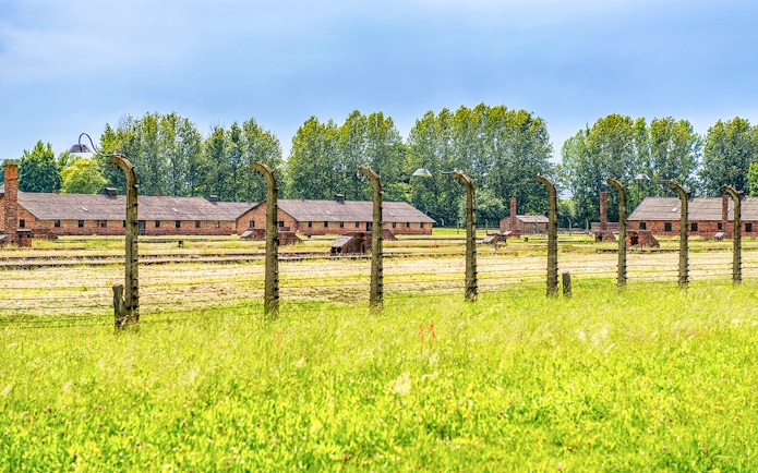 Auschwitz-Birkenau barracks and barbed wire fence under a blue sky, part of Krakow tour.