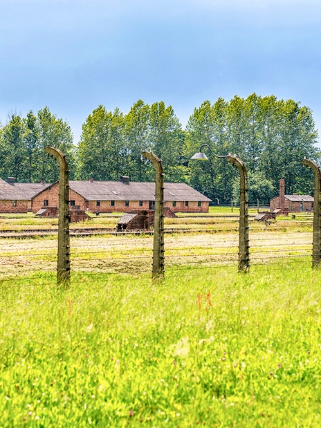 Auschwitz-Birkenau barracks and barbed wire fence under a blue sky, part of Krakow tour.