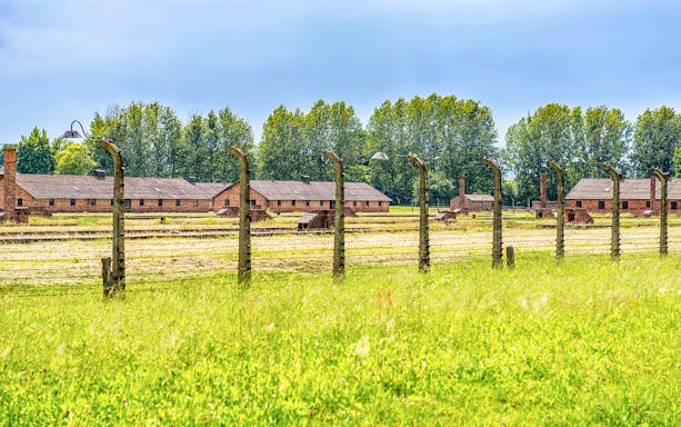 Auschwitz-Birkenau barracks and barbed wire fence under a blue sky, part of Krakow tour.