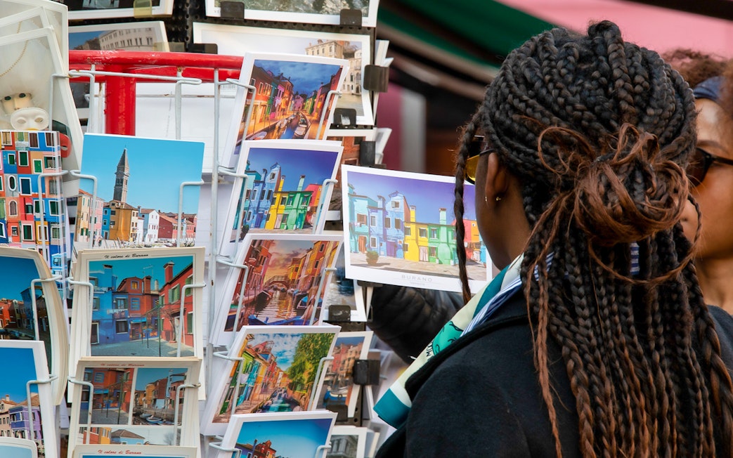 Tourist browsing colorful Burano postcards, Venice museum tour context.