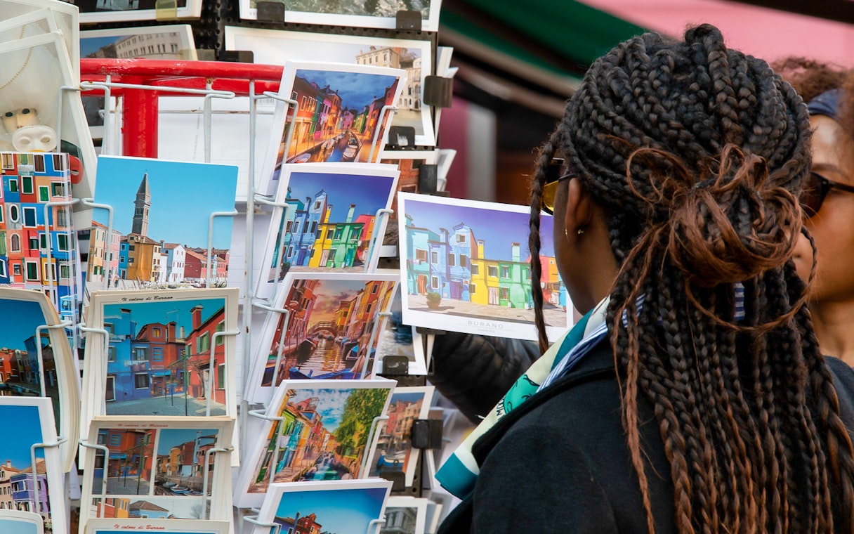 Tourist browsing colorful Burano postcards, Venice museum tour context.