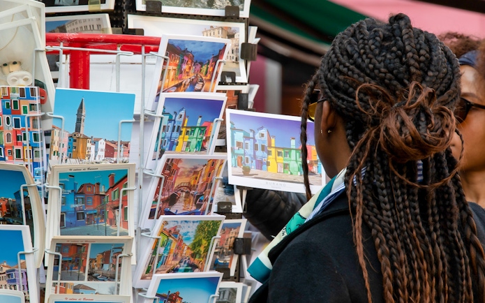 Tourist browsing colorful Burano postcards, Venice museum tour context.