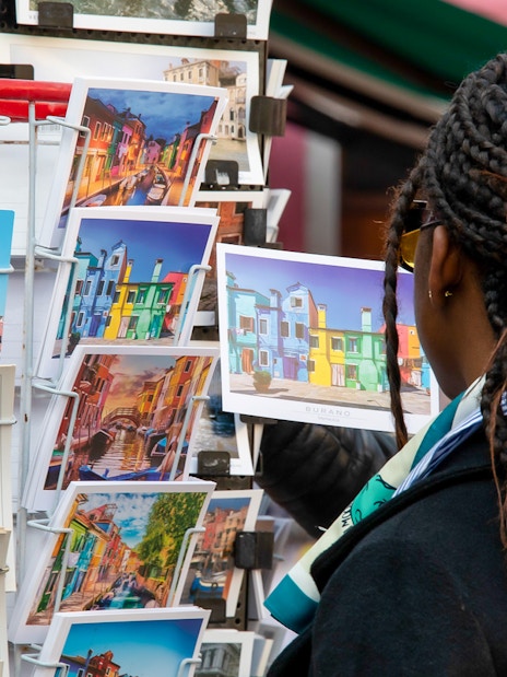 Tourist browsing colorful Burano postcards, Venice museum tour context.