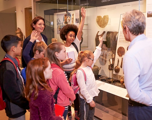 Students observing ancient artifacts in museum display case.
