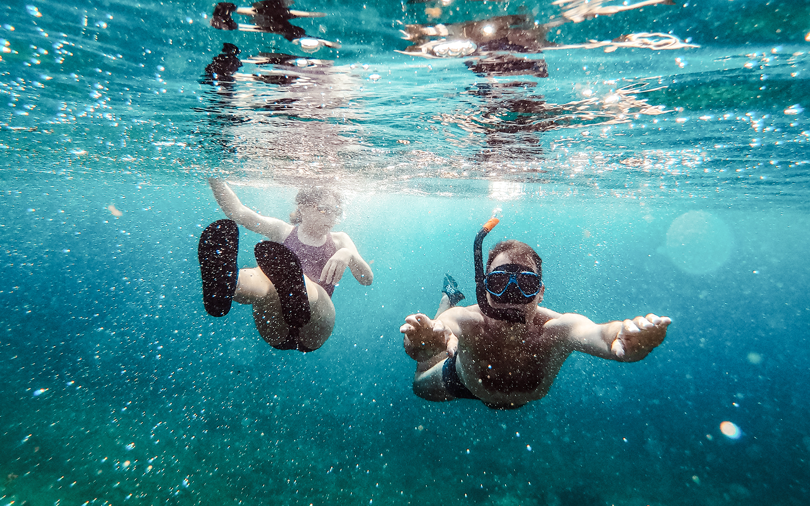 Father and daughter snorkeling underwater in clear blue sea.