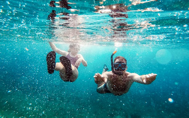 Father and daughter snorkeling underwater in clear blue sea.