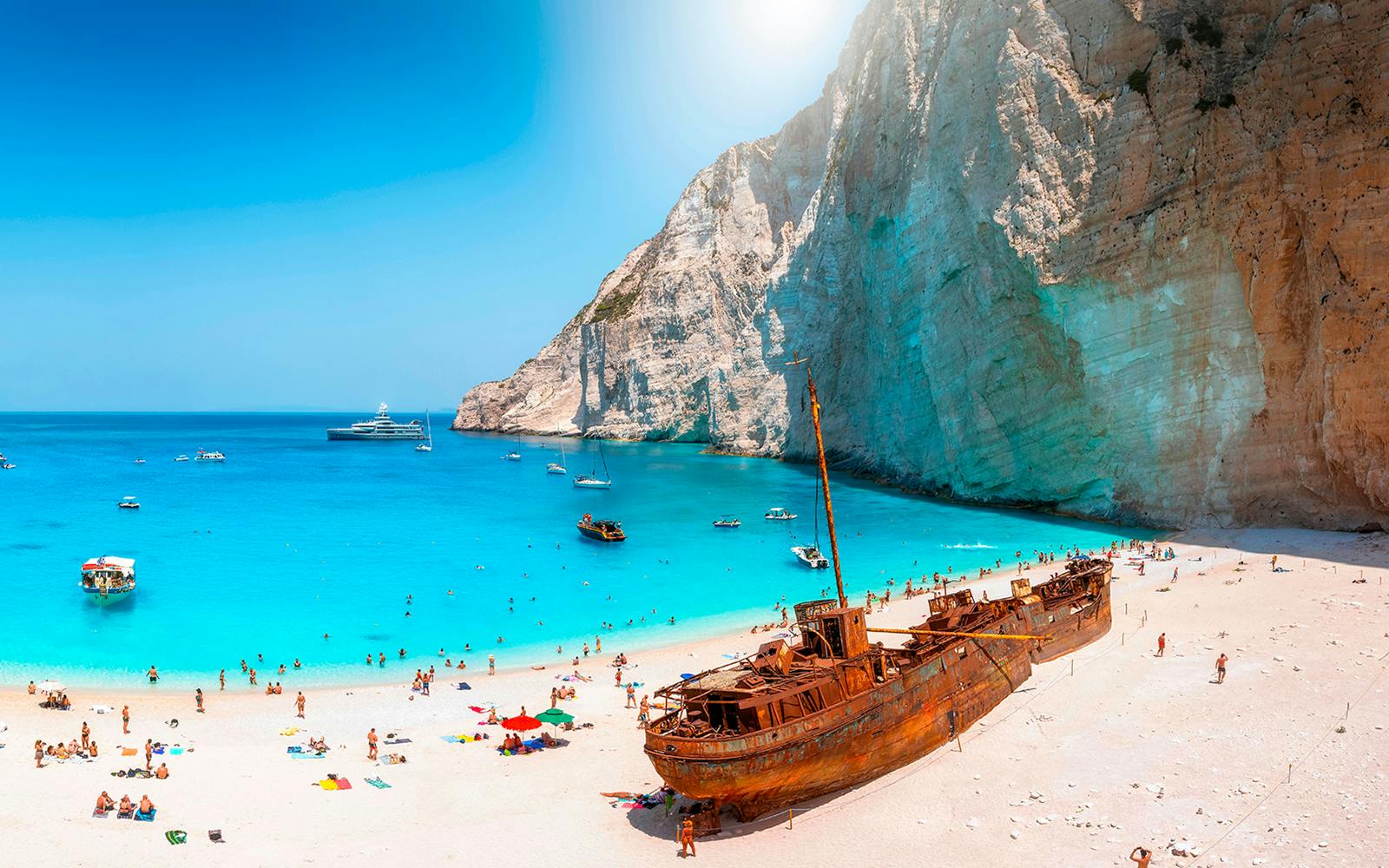 Navagio Beach on Zakynthos with shipwreck, turquoise water, and tourists on the sand.