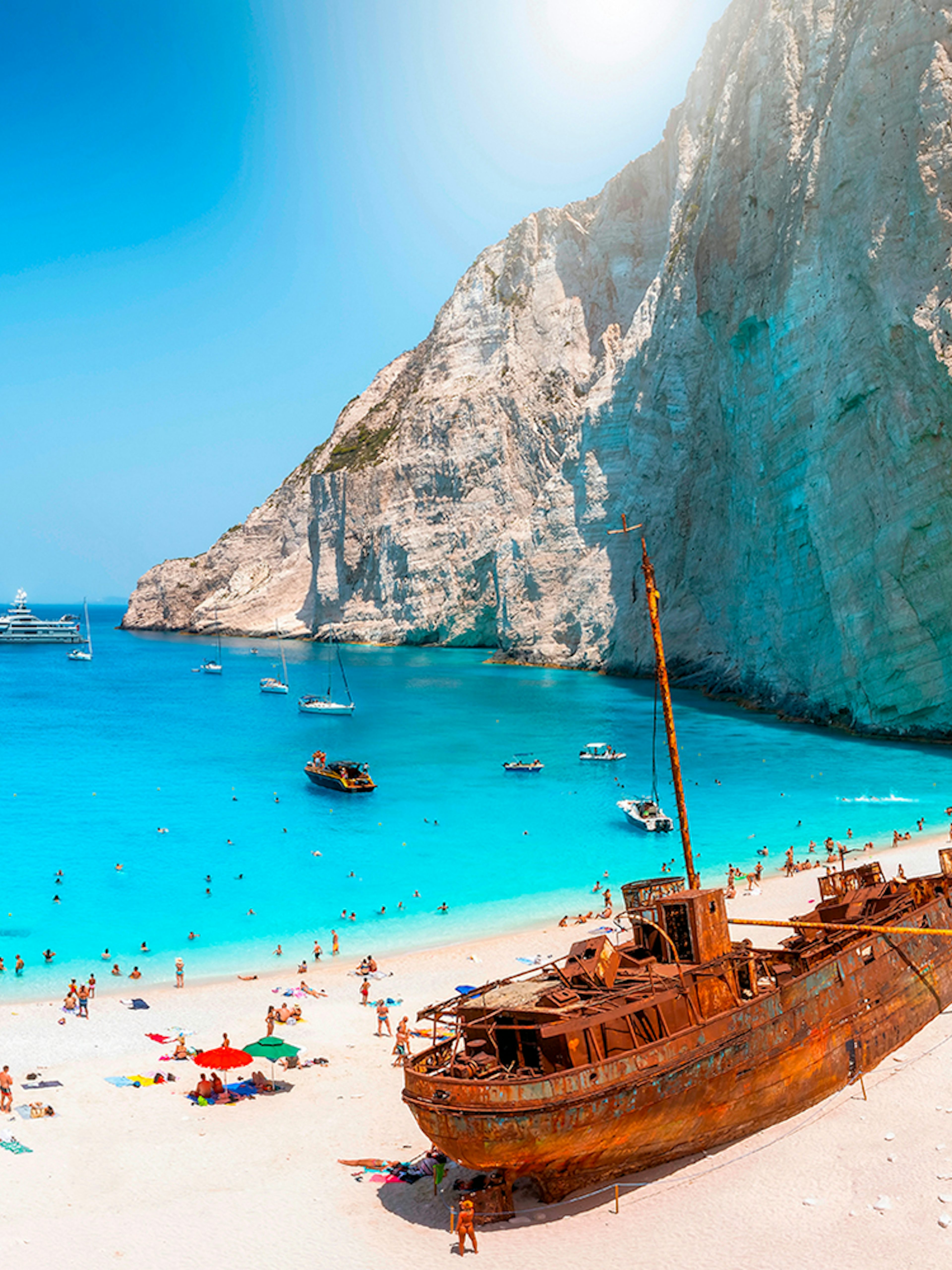 Navagio Beach on Zakynthos with shipwreck, turquoise water, and tourists on the sand.