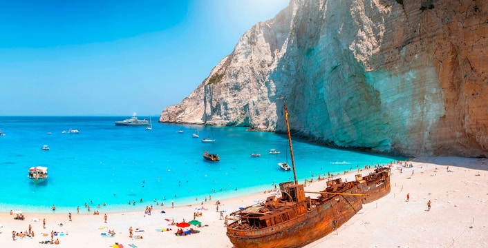 Navagio Beach on Zakynthos with shipwreck, turquoise water, and tourists on the sand.