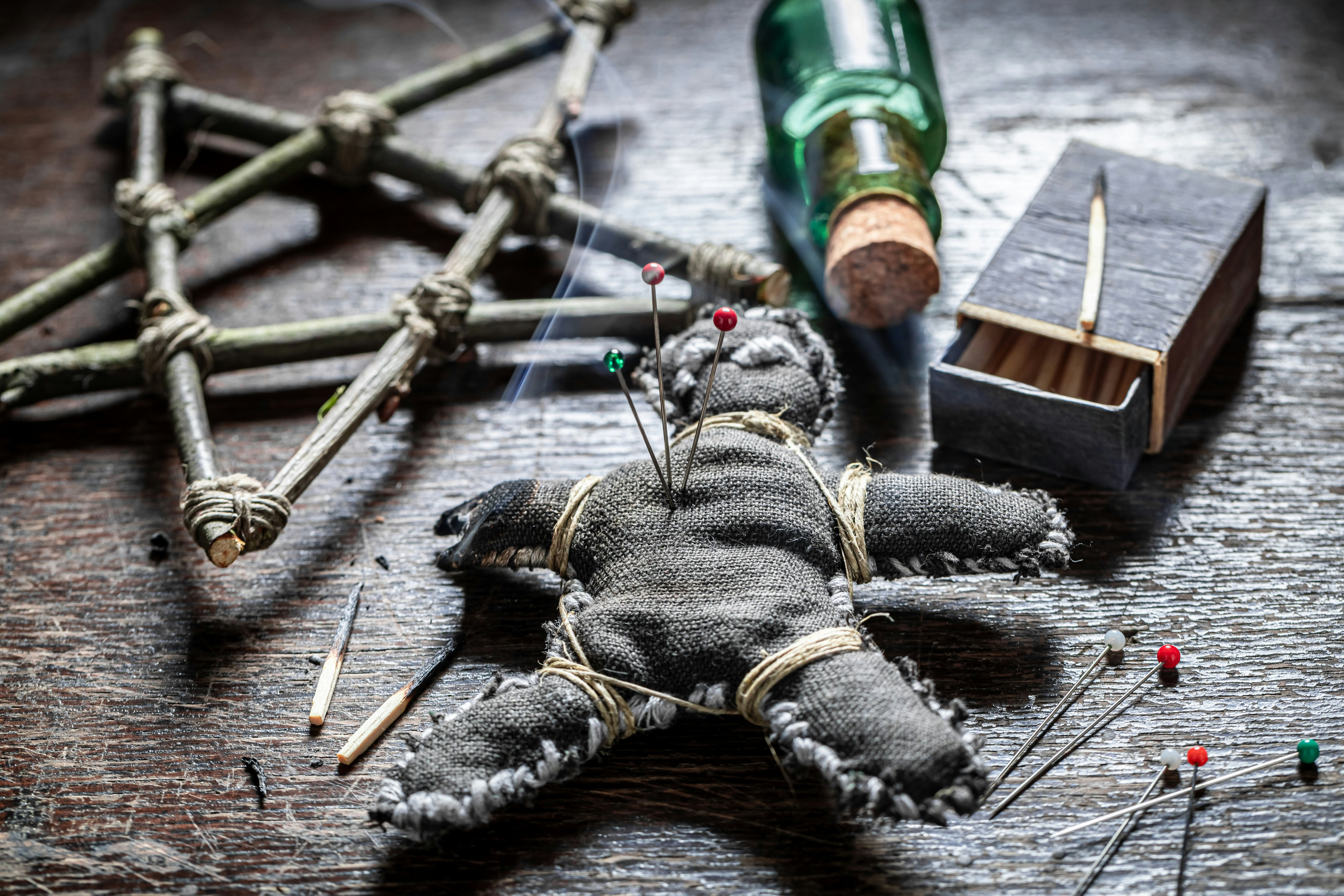 Voodoo doll with pins on a wooden table, surrounded by ritual items.
