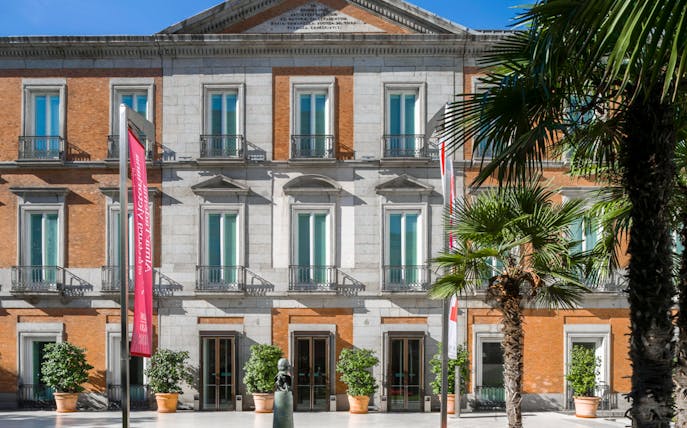 Thyssen-Bornemisza Museum facade with palm trees and banners in Madrid.